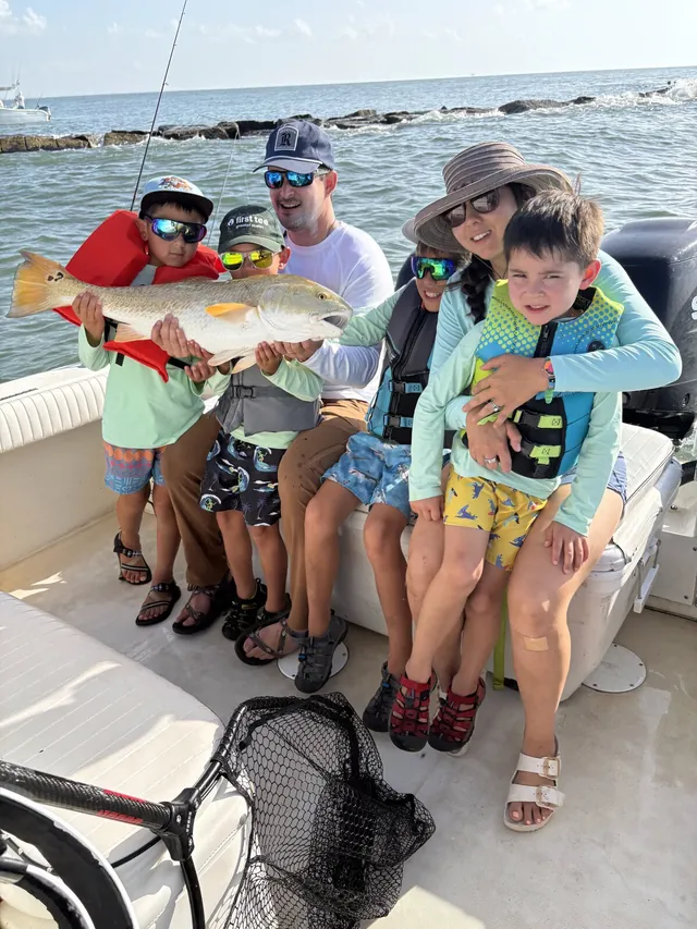 Family aboard Half Time at the Galveston jetties with a large redfish, kids in life jackets