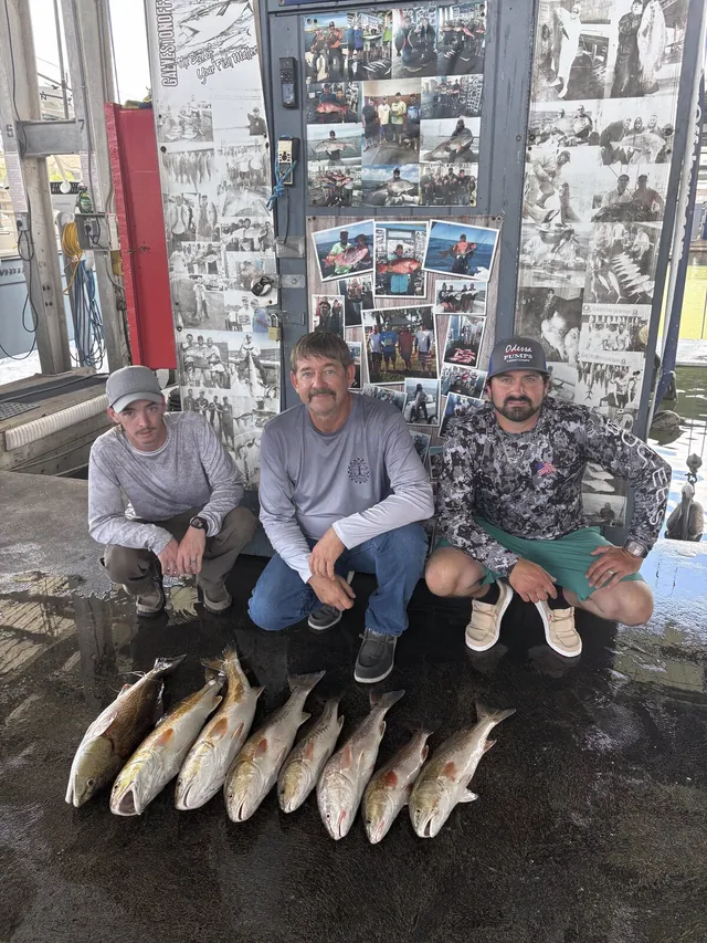Three anglers at the Galveston Offshore dock with a row of speckled trout from a jetty trip