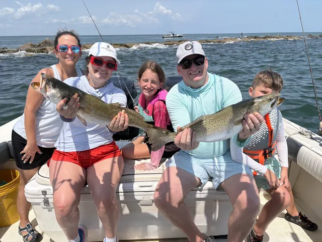 A family holding speckled trout on the deck of the Half Time after a jetty trip