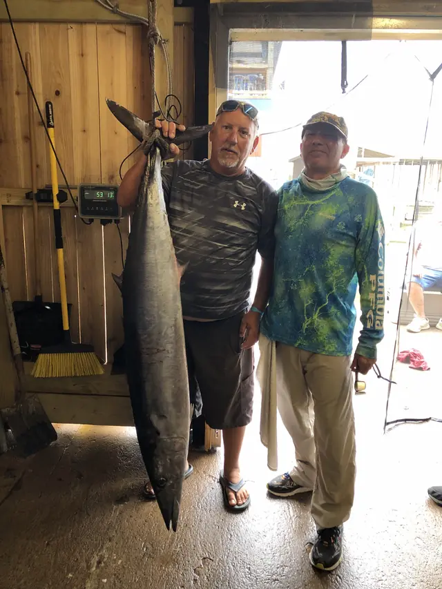 A wahoo hung on the scale at the Galveston dock after a federal offshore trip, two anglers alongside it