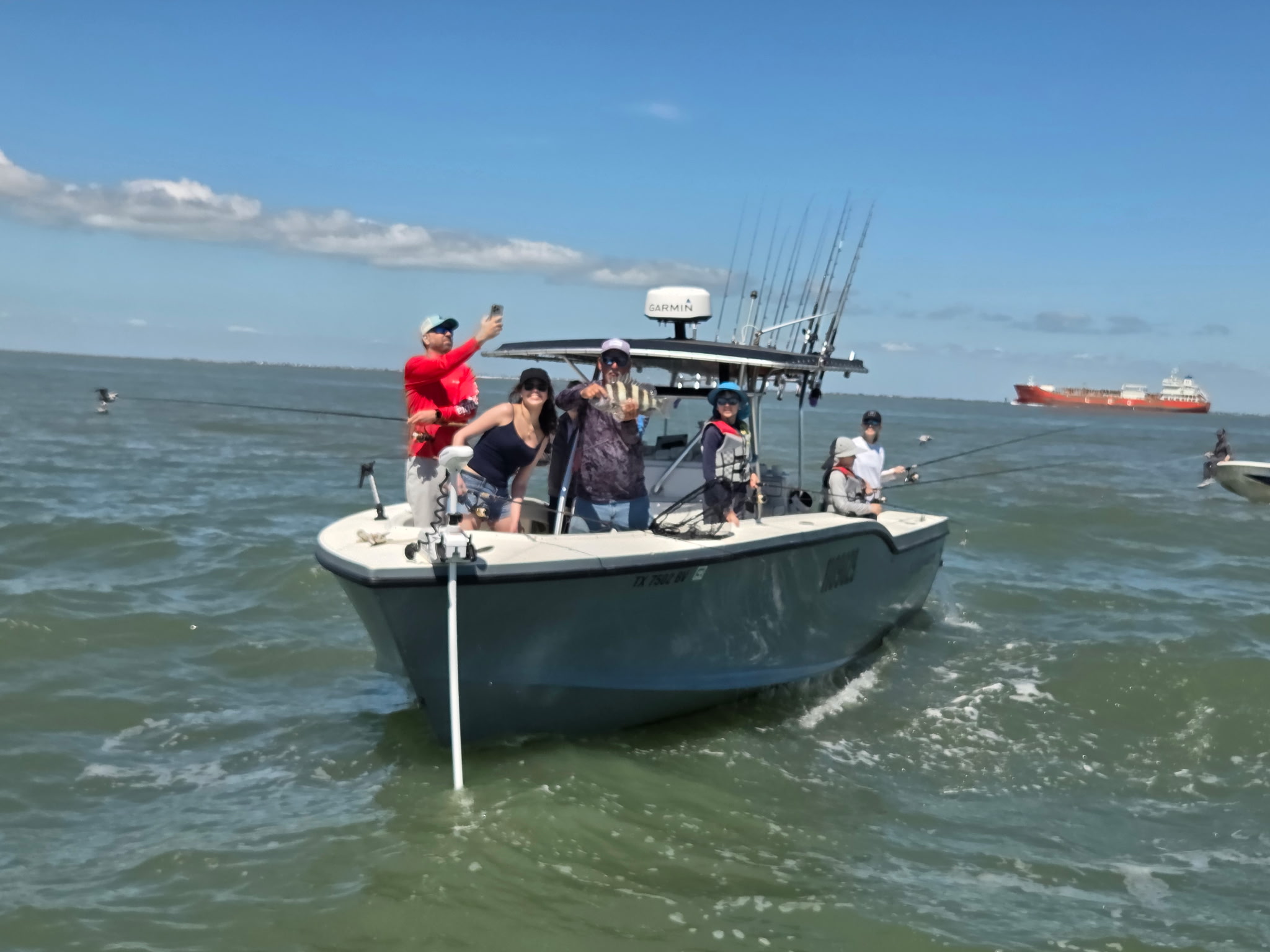 Bow-on shot of Half Time with anglers, Galveston bay water, freighter behind