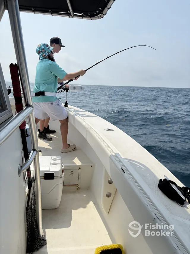 Two anglers actively fishing aboard Half Time, one mid-reel