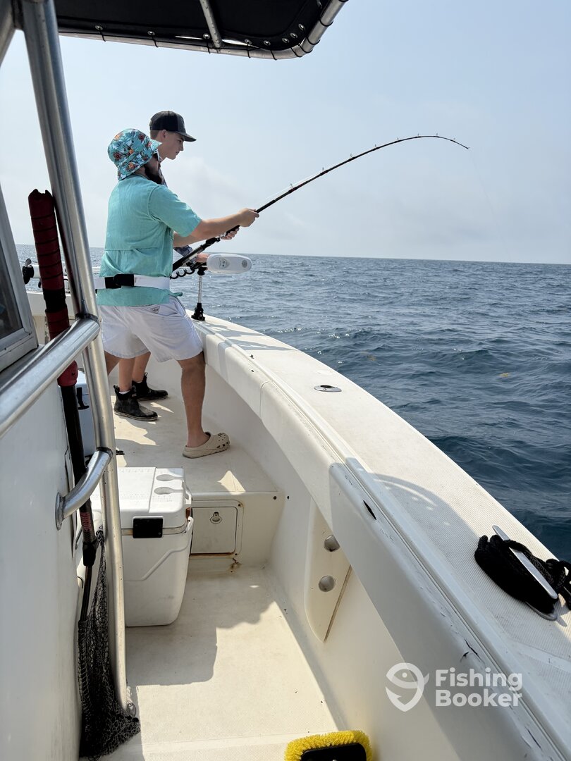 Two anglers actively fishing aboard Half Time, one mid-reel