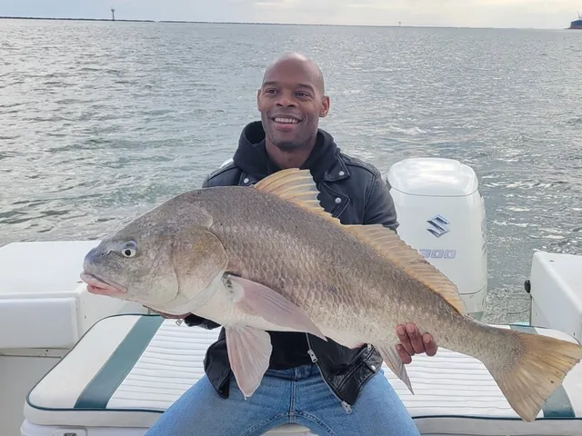 Seated angler holding a healthy redfish caught aboard the boat